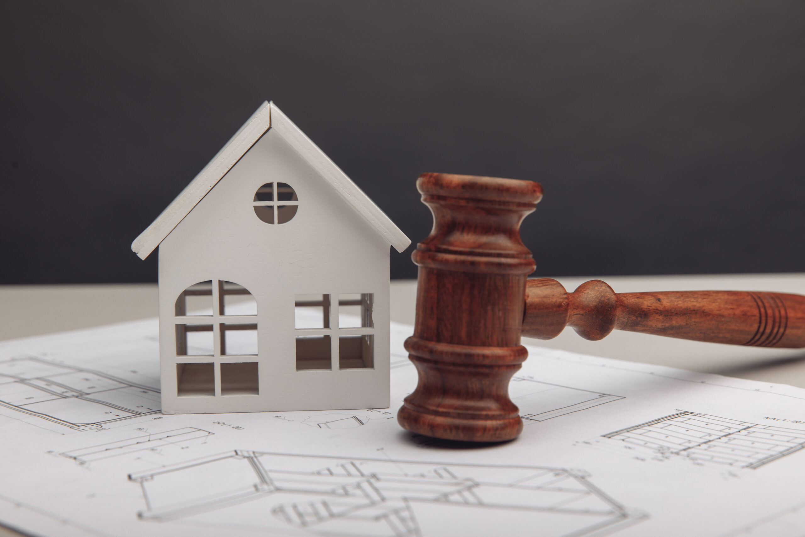 A wooden judge's gavel and a white model house resting on architectural construction blueprints